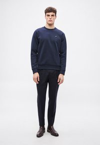 Námornícka mikina s okrúhlym výstrihom a malým logom, kombinovaná s elegantnými tmavými nohavicami a hnedými členkovými čižmami. Hladká textúra, neformálny strih.