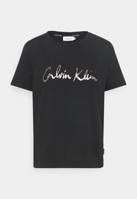 Černé bavlněné tričko s metalickou stříbrnou logem "Calvin Klein" v kurzívě přes celé přední části. Krátké rukávy a kulatý výstřih.
