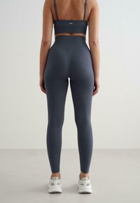 Sivá rebrovaná športová súprava, ktorá obsahuje cropped top a legíny s vysokým pásom, v kombinácii s bielymi športovými topánkami.