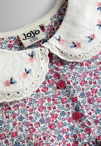 Blusa infantil floral con cuello de encaje blanco, patrones de flores coloridas y botones rosas. La tela es de algodón suave.