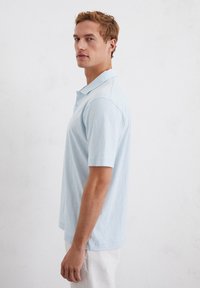 Lichtblauw poloshirt met korte mouwen, kraaghals, subtiele textuur en een rechte zoom, gecombineerd met lichtgekleurde shorts.