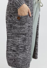 Stickad cardigan i grått och svart med ett strukturerat mönster. Har en knapp på en sidoficka och ribbade manschetter. Avslappnad, ledig passform.