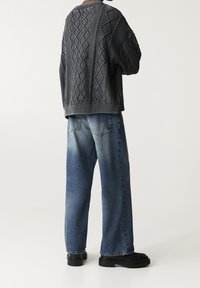 Pull épais gris foncé avec motifs texturés, associé à un jean denim bleu délavé et ample. Des chaussures noires à semelles épaisses complètent la tenue.