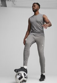 Grijze sportieve tanktop met subtiel patroon, gecombineerd met bijpassende grijze broek met getextureerde accenten, bovenop een zwart-witte voetbal.