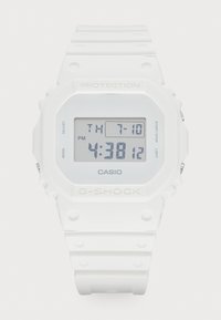 Montre Casio G-Shock numérique blanche avec un bracelet épais, un boîtier arrondi et un grand affichage LCD montrant la date et l'heure en chiffres noirs.
