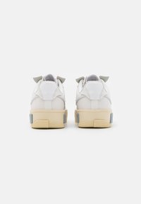 Białe trampki z górną częścią wykonaną z gładkiej skóry, teksturowanymi akcentami i jasnoszarymi detalami. Podeszwa zewnętrzna wykonana z gumy w beżowym kolorze.