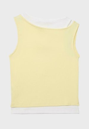 Żółty prążkowany, bezrękawnik typu crop top nałożony na biały top na jasnym, jednolitym tle.