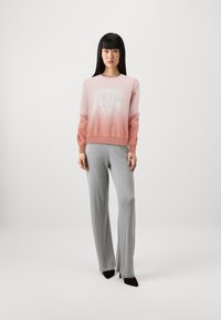 Felpa con gradiente rosa chiaro e logo "GUESS", abbinata a pantaloni grigi a costine e scarpe con tacco nere.