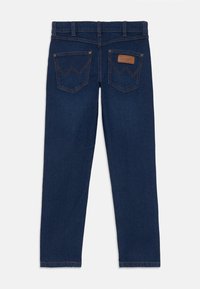 Mörkblå denimjeans med rak skärning, med två bakfickor med triangulär söm och en brun läderlogg ovanför den högra fickan.