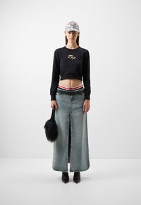 Sudadera negra corta con detalle recortado, falda maxi de mezclilla azul deslavada, botas de tacón negras y un bolso de piel sintética negro. Gorra clara.