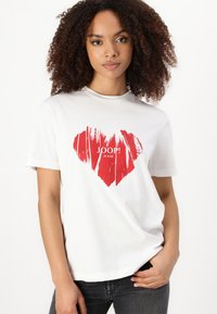 Balta medvilninė marškinėlių maikutė su dideliu raudonu širdies grafiku, turinčiu šepetėlio tekstūrą, o po juo įcentrintas "JOOP! JEANS" logotipas.