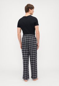 Črna bombažna majica s kratkimi rokavi v kombinaciji s sivimi karirastimi pižamami, ki imajo ohlapen kroj, široke noge in elastičen pas. Brez vidnih dodatkov.
