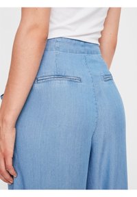 Ljusblå denimbyxor med en figursydd midja, två bakfickor och subtila sömnadsdetaljer. Slät textur, avslappnad design.