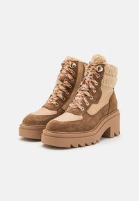 Bottes chelsea en suède marron avec une semelle plateforme beige épaisse, un col en fausse fourrure, des œillets dorés et des lacets à motifs.