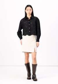 Black lace button-up shirt with scalloped edges, paired with a cream corduroy skirt featuring a side slit, and brown knee-high boots.