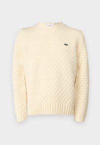 Cream-colored knitted sweater featuring a textured diamond pattern, ribbed cuffs, and hem; includes a small green Lacoste logo on the chest.