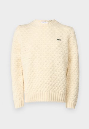Cremfarbener Strickpullover mit strukturiertem Rautenmuster, gerippten Bündchen und Saum; beinhaltet ein kleines grünes Lacoste-Logo auf der Brust.