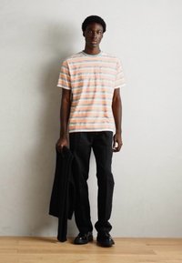 Stribet t-shirt i blødt stof med orange, blå og hvide striber. Sammen med sorte bukser og holder en sort jakke.