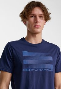 Mörkblå bomullströja med korta ärmar, med en böjd randig grafik i ljusblå och ordet "PRESTANDA" tryckt nedanför.