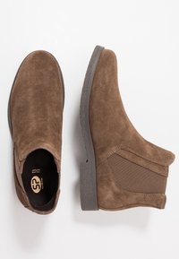 Botines de ante marrón con lados elásticos y suelas de goma, que presentan una puntera redondeada y un acabado texturizado para agarre y comodidad.