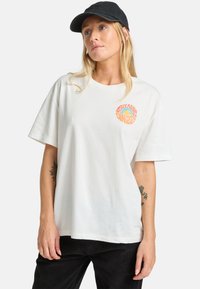 T-shirt bianco in cotone con scollo rotondo e maniche corte, caratterizzato da un design grafico multicolore sul lato sinistro del petto.