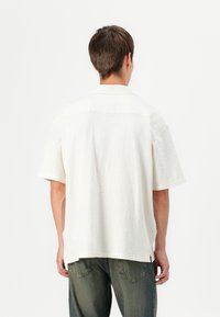 Hvid kortærmet skjorte med struktureret stof og en afslappet pasform. Har en klassisk krave og en lige kant, parret med slidte jeans.