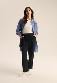 Niebiesko-biała, pasiasta koszula z guzikami nałożona na białą koszulkę, zestawiona z czarnymi spodniami i białymi sneakersami. Miękkie faktury i swobodny krój.