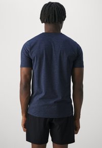T-shirt bleu marine à manches courtes avec un col rond, fabriqué en tissu texturé. Le dos présente une coupe lisse, associé à un short noir.