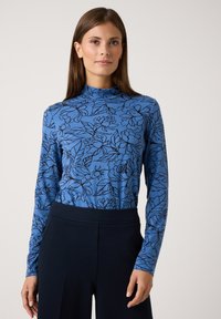Long-sleeve blue top featuring a floral pattern in black, high neck design, soft fabric, paired with dark navy trousers.
