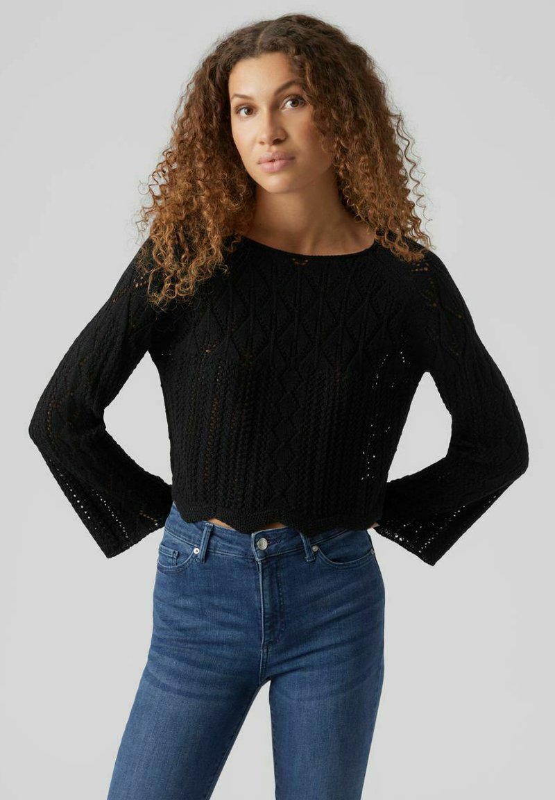 Pull cropped noir avec un motif de tricot texturé, doté de manches longues et d'un col rond, associé à un jean bleu foncé.