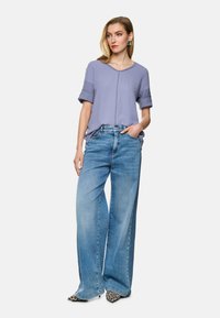 Hellblaues, kurzärmliges Oberteil mit umgeschlagenen Ärmeln, kombiniert mit weiten blauen Jeans aus Denim. Dazu tierisch gemusterte spitze Schuhe.