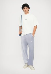 T-shirt de algodão branco com estampa "BONSAI", emparelhada com calças de moletão azul claro com cintura elástica. O modelo segura uma bolsa de alça azul.