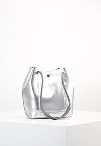 Sac seau en métal argenté avec texture lisse, bords doux, deux poignées et une poche arrière. Design minimaliste sans quincaillerie visible.