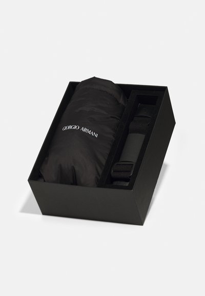 Caja de regalo negra que contiene una chaqueta de plumas negra y un cinturón. La chaqueta es lisa con detalles del logo; la caja tiene un acabado mate.