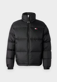 Svart puffjakke med høy krage, frontlukking med glidelås, og horisontale kvilte seksjoner. Har en liten logo på brystet.