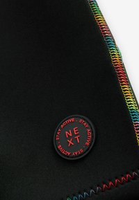 Tissu de sport noir avec des coutures multicolores le long du bord. Présente un logo circulaire avec "NEXT" en texte rouge.
