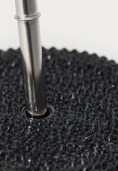 Black decorative base with a textured surface of faceted shapes; a metallic pole emerges from a central hole, showcasing a sleek design.