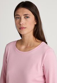 Lichtroze langemouwen top met een ronde halslijn, gemaakt van zachte stof. Heeft een eenvoudig, strak ontwerp zonder zichtbare patronen of accenten.