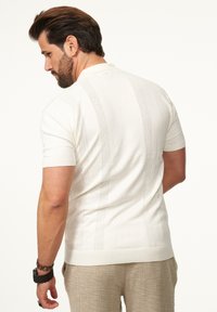 Gestricktes Polohemd mit kurzen Ärmeln in Off-White, mit strukturierten vertikalen Streifen und einem gerippten Kragen. Weiches Material mit einer schmalen Passform.