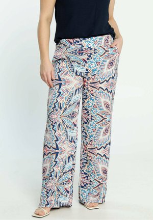 Mujer con pantalones de pierna ancha con patrones geométricos florales en azul, blanco y rosa, combinados con una blusa negra y sandalias blancas.