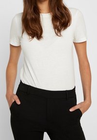 T-shirt blanc à manches courtes avec un col rond, fabriqué en tissu doux, associé à un pantalon noir tailleur avec une finition lisse et des poches.