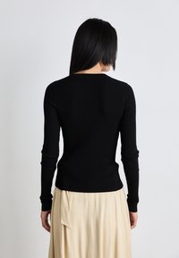 Melnas ribotu piedurkņu blūze ar apaļu kakla izgriezumu, pieguļoša silueta un teksturēta auduma. Kombinēta ar plūstošu beidža krāsas svārku.