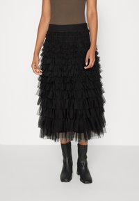 Black tiered tulle skirt with ruffled layers, elastic waistband, and mid-calf length. Paired with sleek black ankle boots.