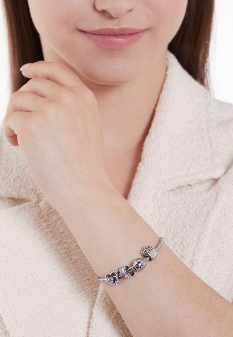 Zilveren armband met bedeltjes, featuring hartvormige en decoratieve kralen met ingewikkelde ontwerpen, tentoongesteld op een pols gekleed in een lichtgekleurde trui.