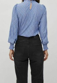 Sininen paita, jossa on silmukkakuvio, joustavat puffihihat ja avainreikätakki, yhdistettynä mustiin istuviin farkkuihin, joissa on takataskut.