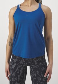 Canotta sportiva blu con spalline sottili e scollo rotondo, con un logo grigio. Abbinata a leggings neri con motivo.