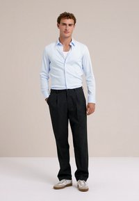 Világoskék gombos ing, fehér alsóing, sötét nadrág és bézs sportcipő. Finom anyag, testre szabott fazon és klasszikus dizájn.