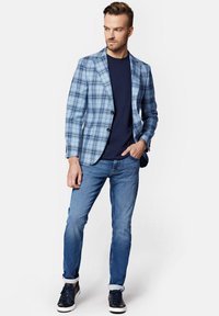 Marynarka w niebiesko-białą kratę, na pojedynczy guzik, zestawiona z granatową koszulą i jasnoniebieskimi dżinsami. W zestawie sportowe buty.