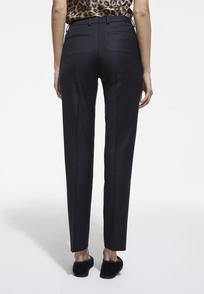Schwarze, taillierte Hose mit schlanker Passform, ausgestattet mit zwei Gesäßtaschen und einer glatten Textur. Kombiniert mit einem Top im Leopardenmuster.