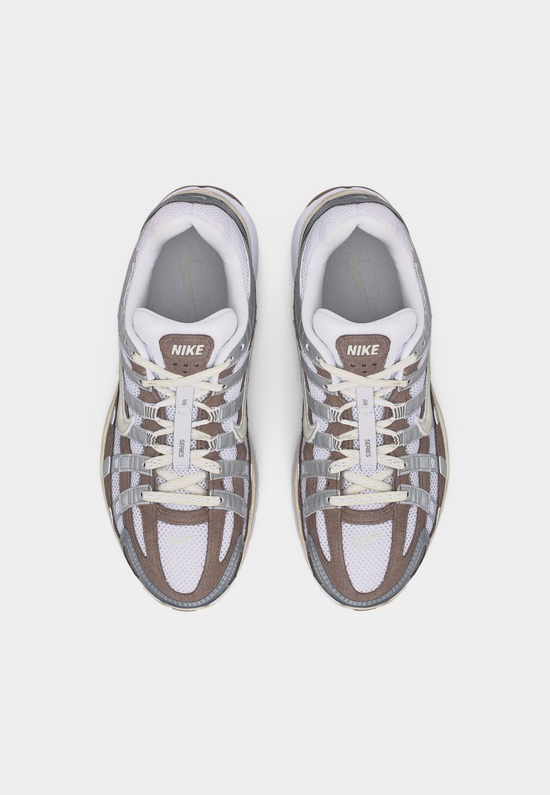 Paire de chaussures de course Nike blanches et grises avec des accents beige et des lacets, vues de dessus sur un fond blanc uni.